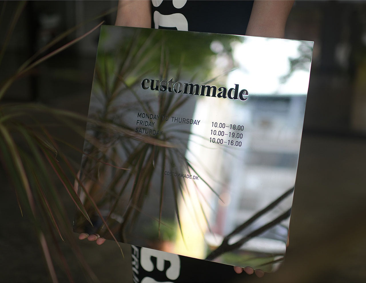 Side profile showing the solid 2mm thickness and polished edges of the mirror stainless steel signage held by hand