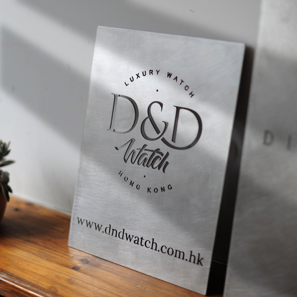 Handcrafted stainless steel brand plaque displayed on a wooden surface, showing light diffusion on the vibration finish