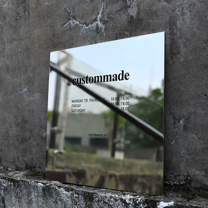 Square mirror polished stainless steel sign mounted on a concrete wall, reflecting the sky and surroundings for a modern architectural look