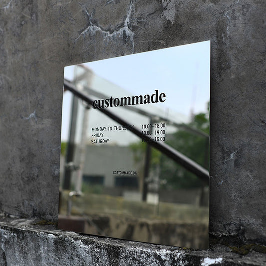 Square mirror polished stainless steel sign mounted on a concrete wall, reflecting the sky and surroundings for a modern architectural look