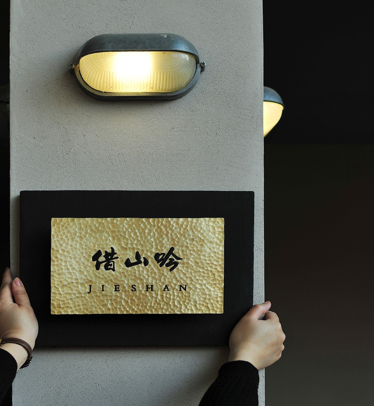 Wall mounted entrance sign held by hands for size reference.